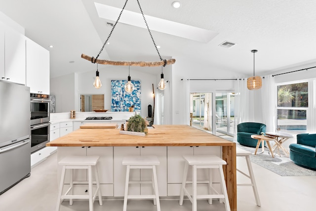 kitchen with white cabinets, appliances with stainless steel finishes, vaulted ceiling with skylight, and a kitchen breakfast bar