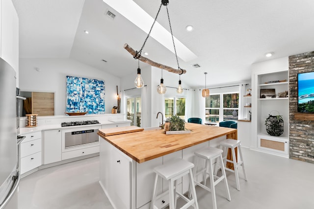 kitchen featuring white cabinets, lofted ceiling, wooden counters, a center island with sink, and built in shelves