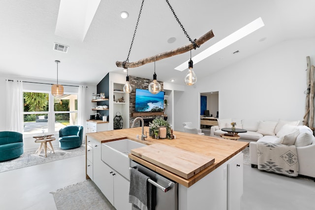 kitchen featuring a center island with sink, vaulted ceiling with skylight, butcher block countertops, white cabinets, and sink