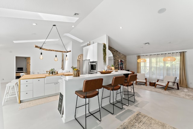 kitchen with white cabinetry, a kitchen bar, decorative light fixtures, and vaulted ceiling