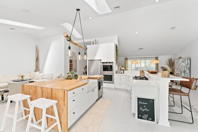 kitchen featuring appliances with stainless steel finishes, pendant lighting, a skylight, white cabinets, and a kitchen breakfast bar