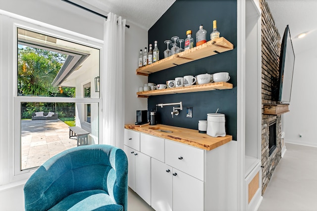 bar featuring a fireplace, sink, white cabinets, wooden counters, and a textured ceiling