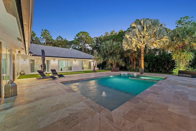 pool at dusk featuring a patio and an in ground hot tub