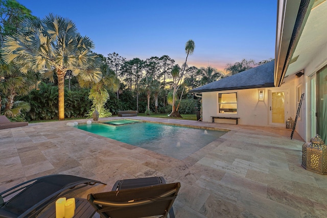 pool at dusk featuring a patio area and an in ground hot tub