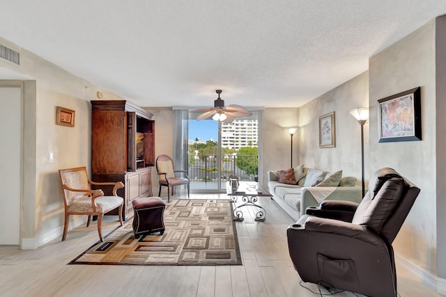 living room with a textured ceiling, light wood-type flooring, and ceiling fan