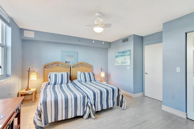 bedroom with a textured ceiling, light wood-type flooring, and ceiling fan