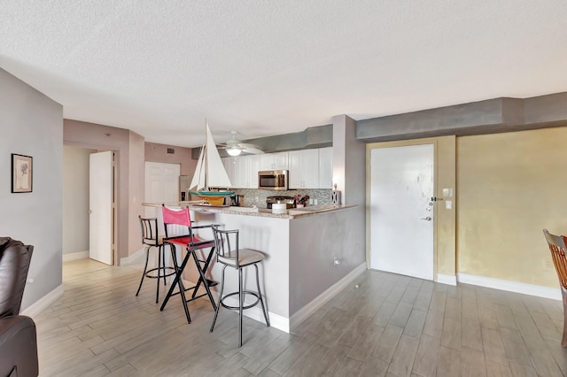 kitchen featuring a kitchen breakfast bar, kitchen peninsula, light hardwood / wood-style floors, white cabinetry, and stainless steel appliances