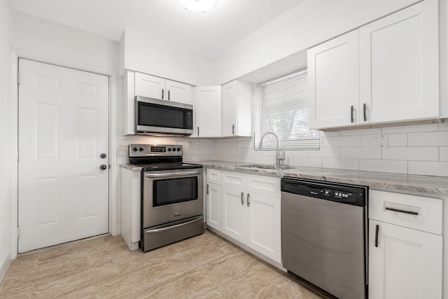 kitchen with light stone countertops, appliances with stainless steel finishes, tasteful backsplash, sink, and white cabinetry