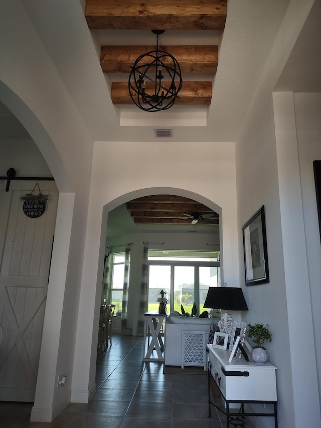 hallway with dark tile patterned flooring, beam ceiling, a barn door, and a tray ceiling