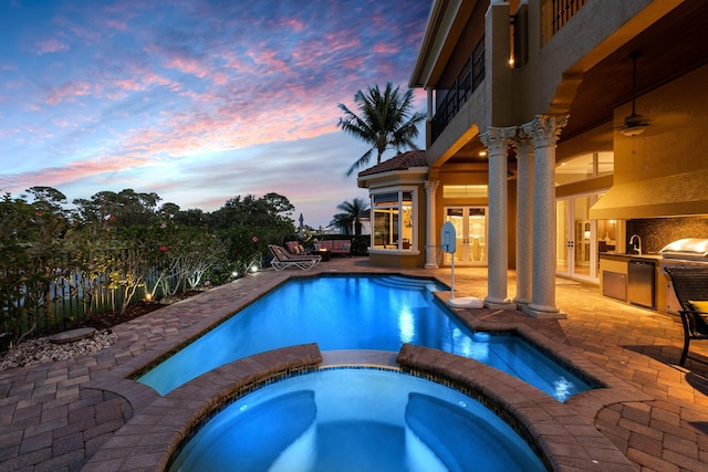 pool at dusk featuring an in ground hot tub, french doors, area for grilling, exterior kitchen, and a patio area