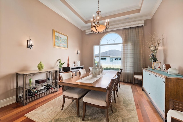 dining area with a tray ceiling, crown molding, hardwood / wood-style floors, and an inviting chandelier