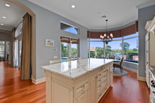 kitchen featuring light stone countertops, crown molding, pendant lighting, hardwood / wood-style floors, and a center island