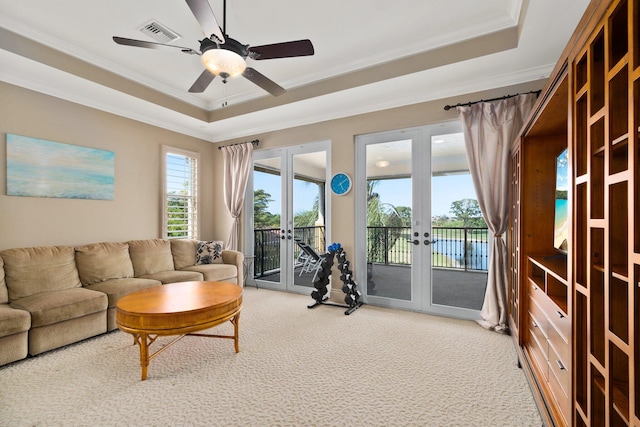 living room featuring ceiling fan, french doors, a tray ceiling, carpet, and ornamental molding