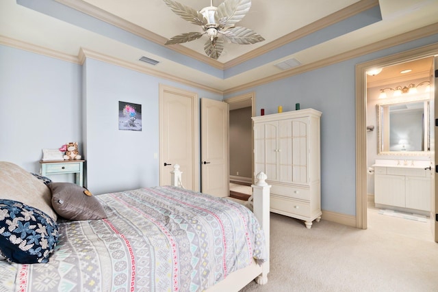 bedroom with crown molding, ensuite bath, ceiling fan, a tray ceiling, and light colored carpet