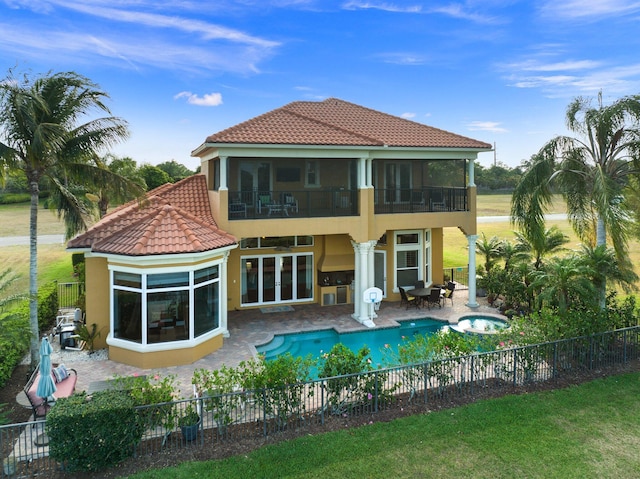 rear view of property featuring a swimming pool with hot tub, a balcony, and a patio