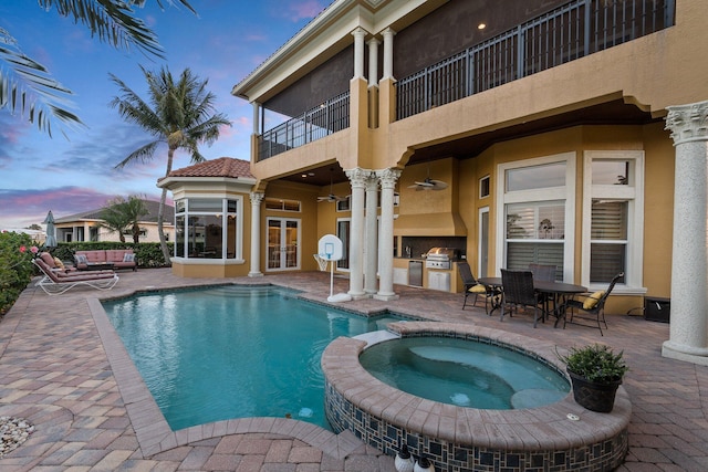 pool at dusk featuring a grill, an in ground hot tub, a patio, and an outdoor kitchen