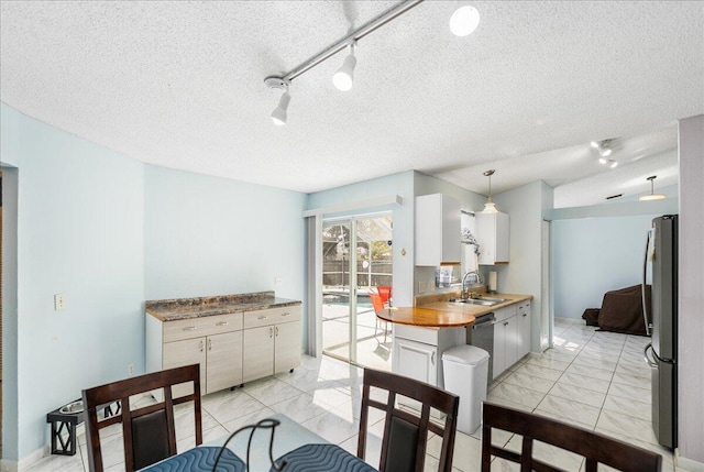 kitchen with track lighting, sink, decorative light fixtures, white cabinetry, and stainless steel refrigerator