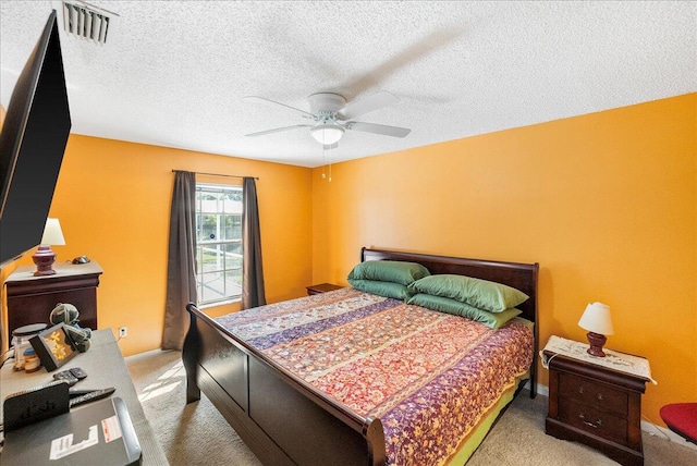 bedroom with ceiling fan, light colored carpet, and a textured ceiling