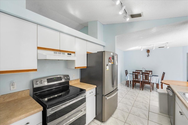 kitchen with rail lighting, vaulted ceiling, a textured ceiling, appliances with stainless steel finishes, and white cabinetry