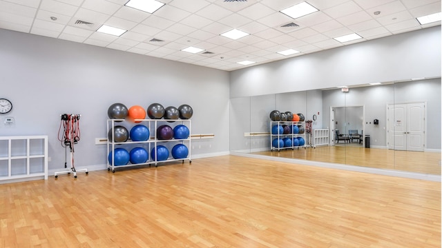 exercise room with a drop ceiling, light wood-type flooring, and a high ceiling