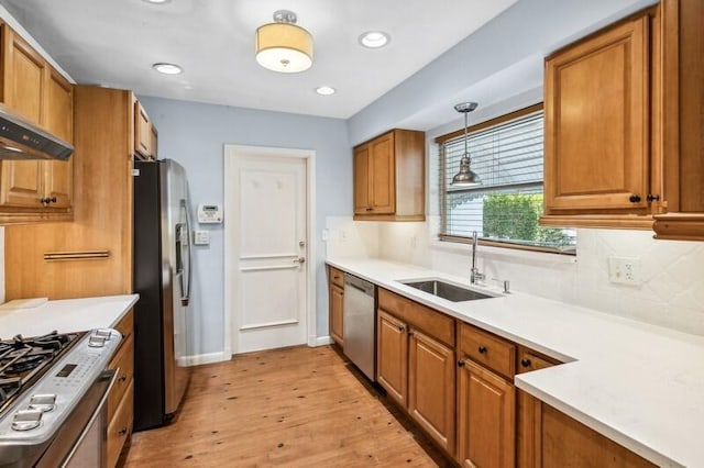 kitchen with premium range hood, stainless steel appliances, sink, pendant lighting, and light hardwood / wood-style floors