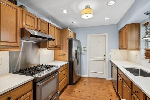 kitchen featuring sink, hanging light fixtures, light wood-type flooring, appliances with stainless steel finishes, and tasteful backsplash