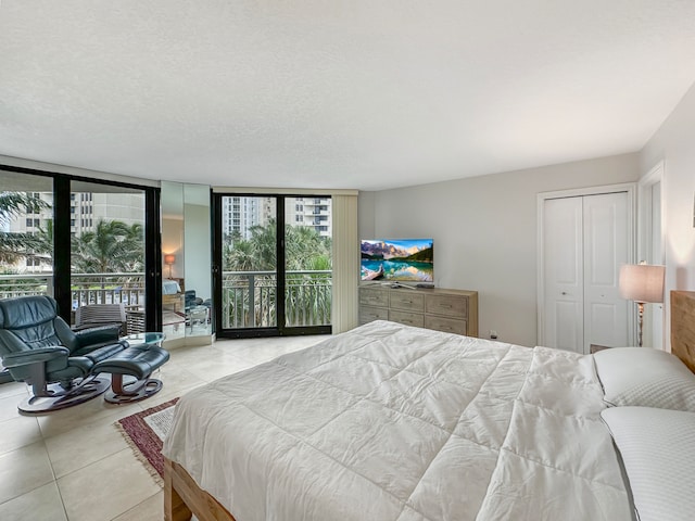 bedroom featuring access to exterior, a textured ceiling, light tile patterned flooring, a wall of windows, and a closet