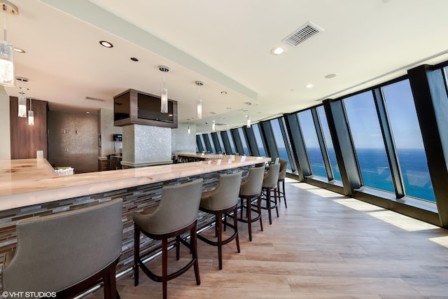 kitchen with hanging light fixtures, backsplash, light hardwood / wood-style floors, a kitchen bar, and a water view