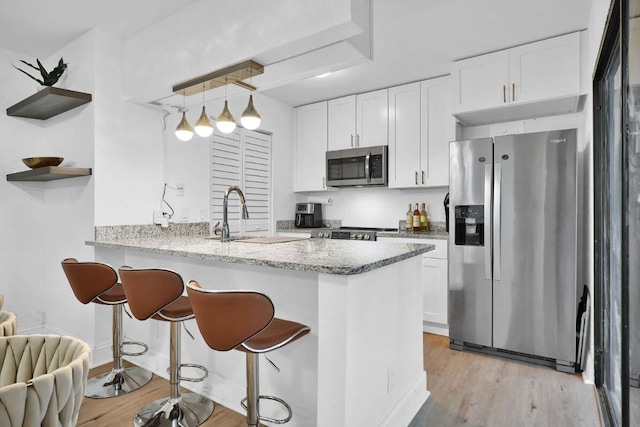 kitchen featuring kitchen peninsula, appliances with stainless steel finishes, pendant lighting, light hardwood / wood-style flooring, and white cabinets