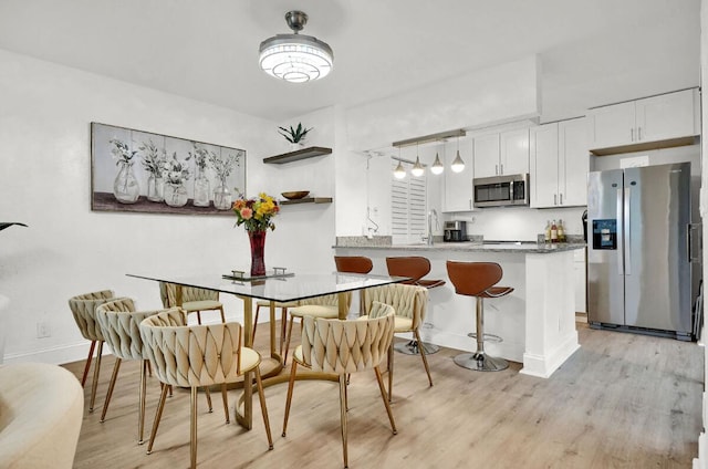 kitchen featuring white cabinetry, kitchen peninsula, a breakfast bar, appliances with stainless steel finishes, and light wood-type flooring