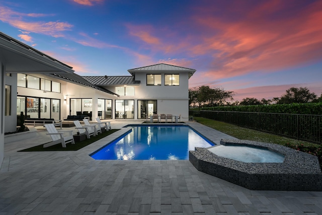 pool at dusk with outdoor lounge area, a patio area, and an in ground hot tub