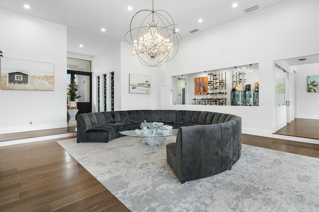 living room featuring dark hardwood / wood-style flooring, a towering ceiling, indoor bar, and an inviting chandelier