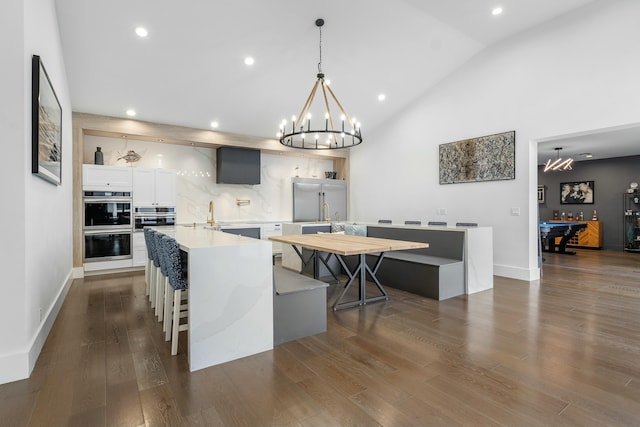 kitchen featuring dark wood-type flooring, a center island with sink, a kitchen breakfast bar, white cabinets, and hanging light fixtures