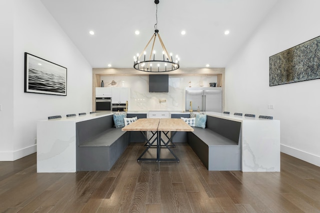 dining area with high vaulted ceiling, dark wood-type flooring, and a notable chandelier