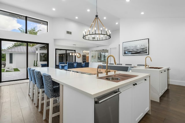 kitchen featuring dark hardwood / wood-style flooring, high vaulted ceiling, decorative light fixtures, a center island with sink, and white cabinets