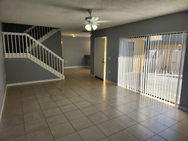 empty room with ceiling fan, light tile patterned floors, and a textured ceiling