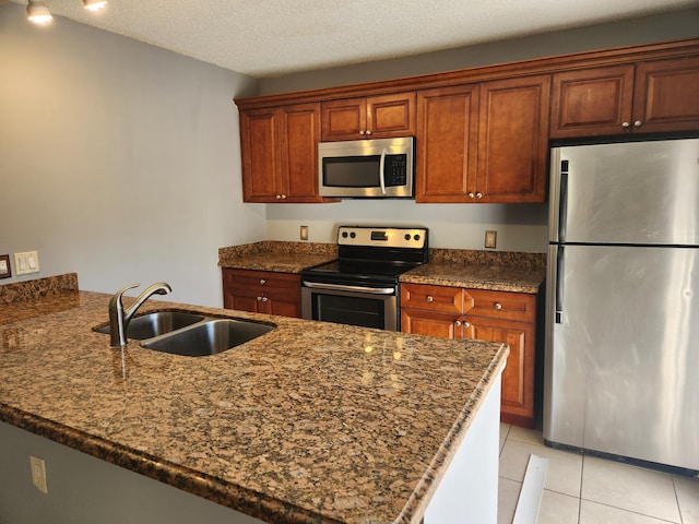 kitchen with kitchen peninsula, appliances with stainless steel finishes, dark stone counters, a textured ceiling, and sink