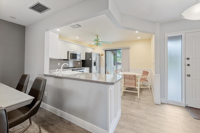 kitchen featuring kitchen peninsula, light hardwood / wood-style floors, white cabinetry, and stainless steel appliances