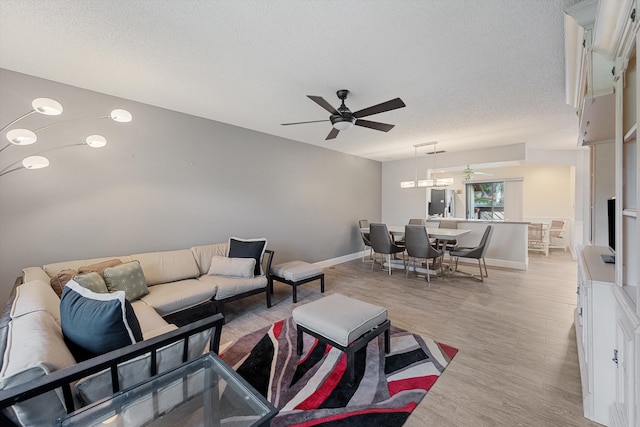 living room featuring ceiling fan, light hardwood / wood-style floors, and a textured ceiling