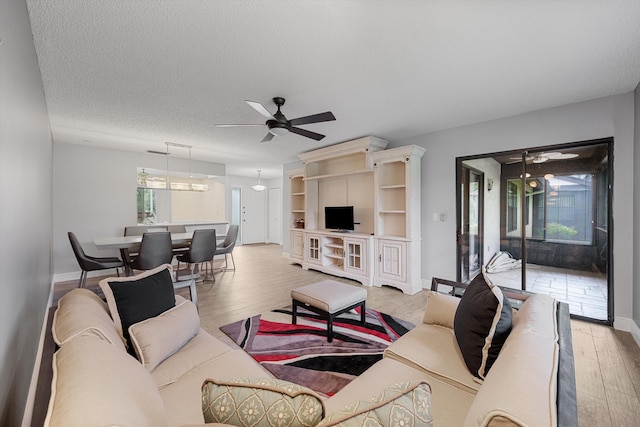 living room with ceiling fan, a textured ceiling, and light wood-type flooring