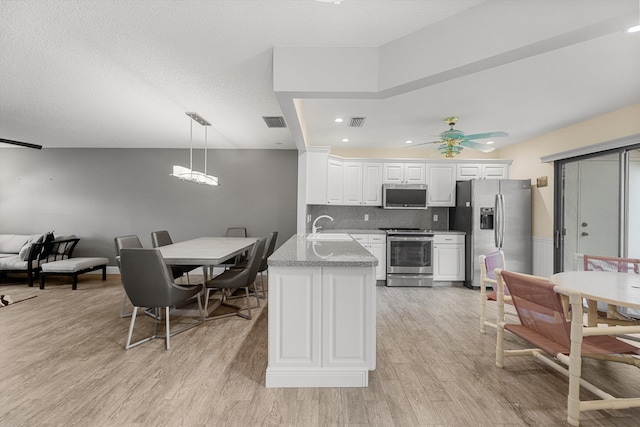 kitchen with appliances with stainless steel finishes, light stone counters, sink, decorative light fixtures, and light hardwood / wood-style flooring