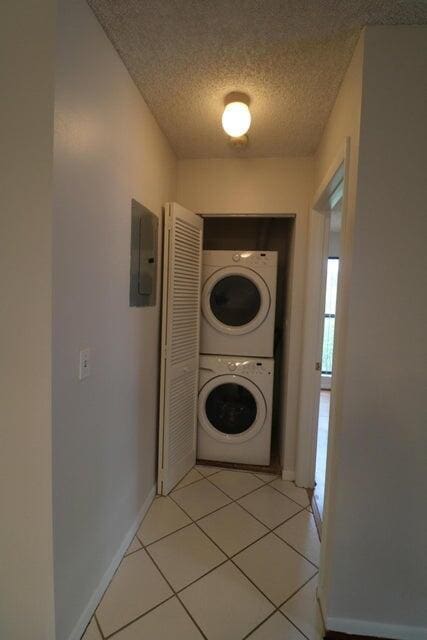 laundry room with a textured ceiling, electric panel, stacked washer / dryer, and plenty of natural light