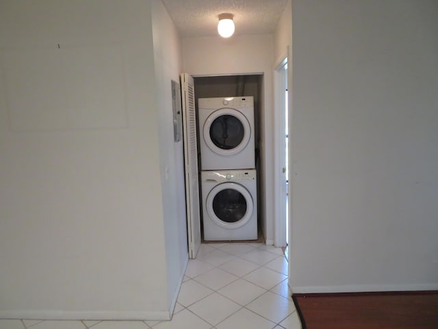 laundry area with light tile patterned floors, a textured ceiling, and stacked washer / dryer