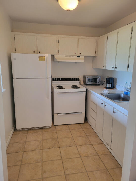 3300 Springdale Blvd, Palm Springs, FL 33461 - kitchen featuring white appliances, under cabinet range hood, a sink, light countertops, and white cabinets