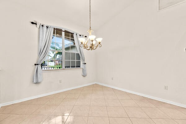 tiled empty room with lofted ceiling and an inviting chandelier