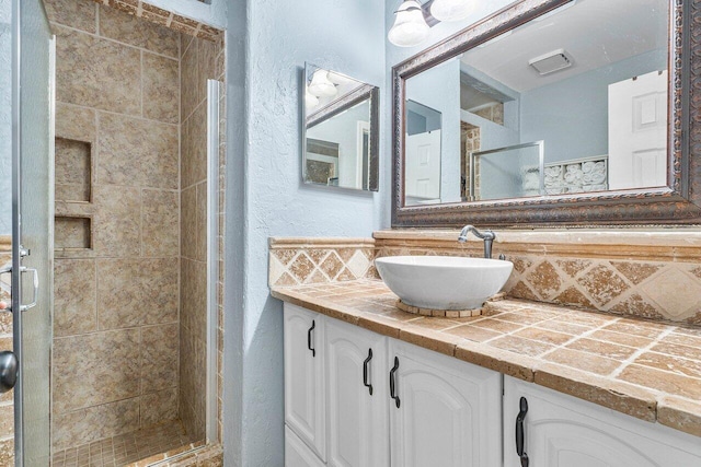 bathroom with vanity, a tile shower, and backsplash