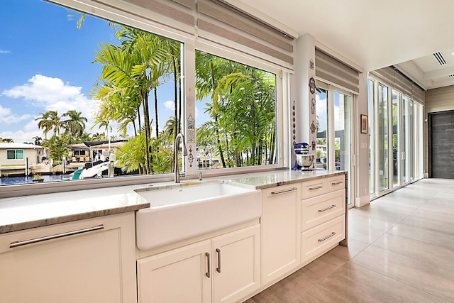 kitchen with white cabinets, light stone counters, light tile patterned floors, and sink