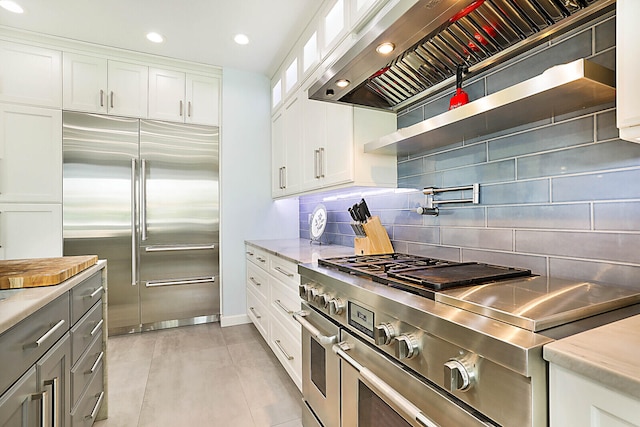 kitchen featuring backsplash, wall chimney range hood, light tile patterned floors, premium appliances, and white cabinetry