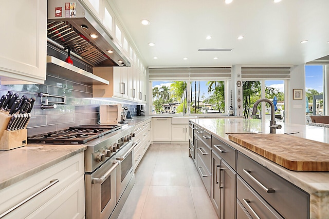 kitchen featuring stainless steel range, white cabinetry, a healthy amount of sunlight, and range hood