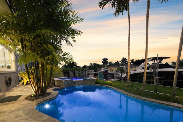 pool at dusk featuring an in ground hot tub and a patio